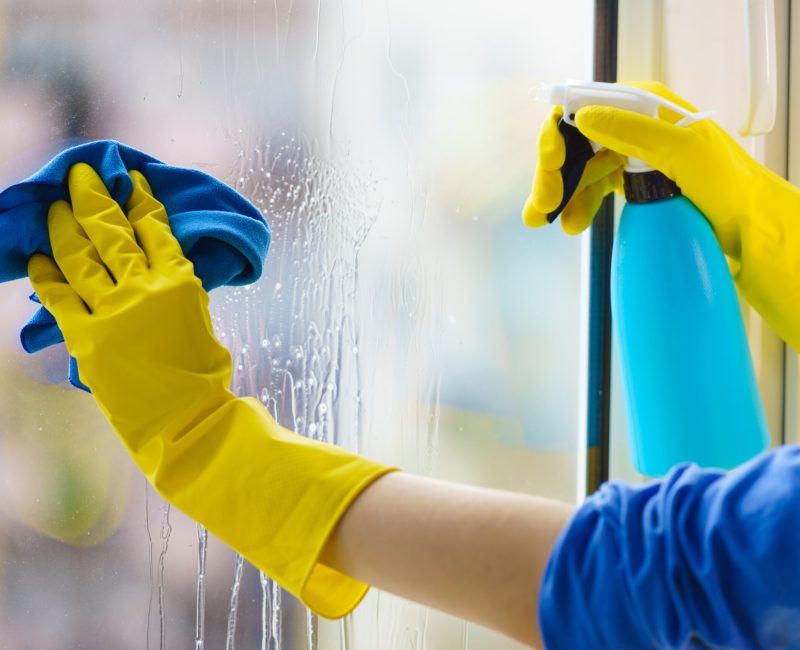 Female hand in yellow gloves cleaning window pane with rag and spray detergent. Cleaning concept